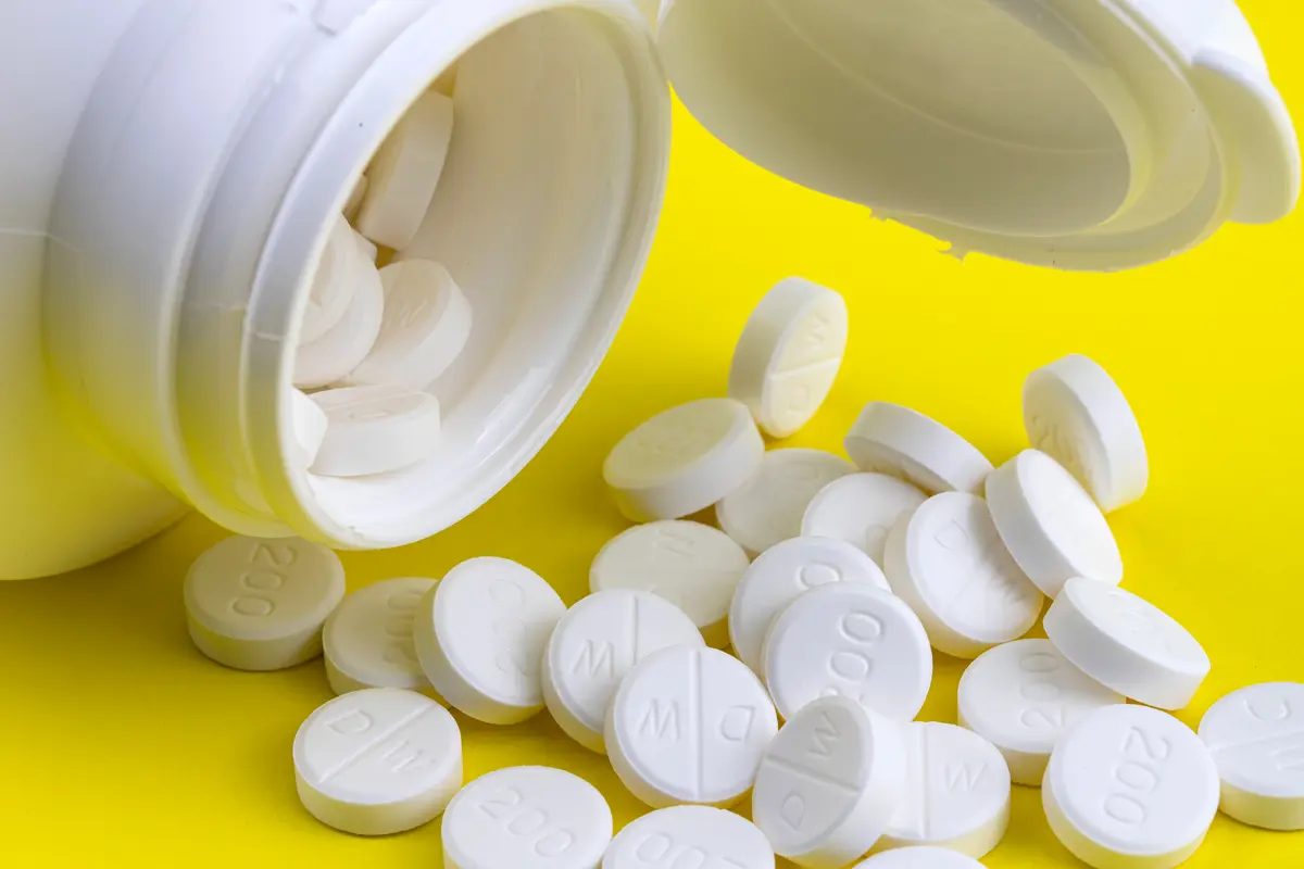 An open bottle of prescription pills on its side against a yellow background