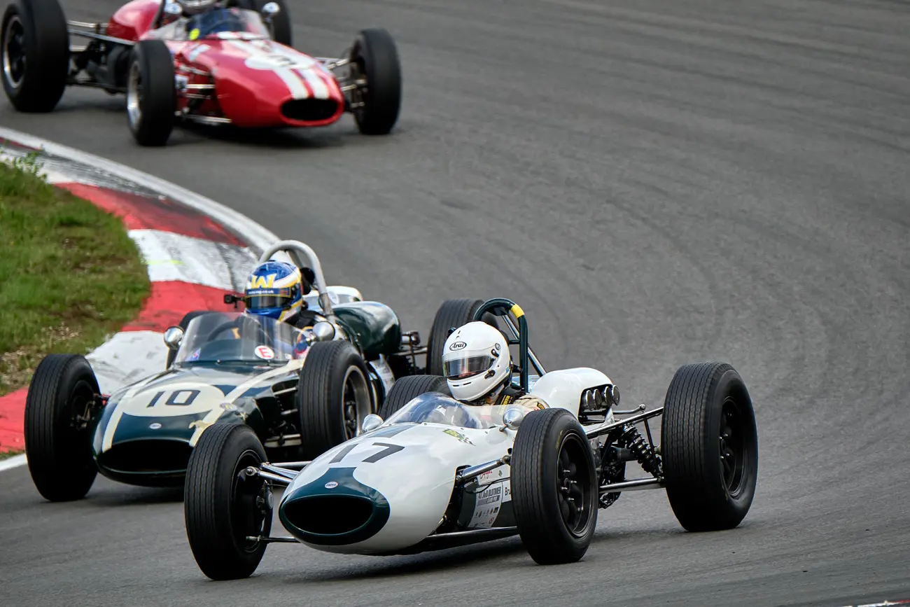 A close up of a corner of the race track with 3 classic formula 1 cars racing