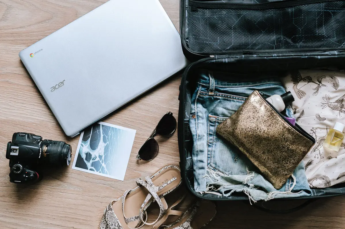 An open suitcase being packed with a laptop and camera next to it