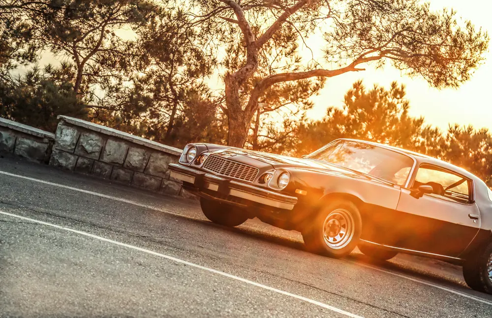 A classic American car parked in a car park at golden hour