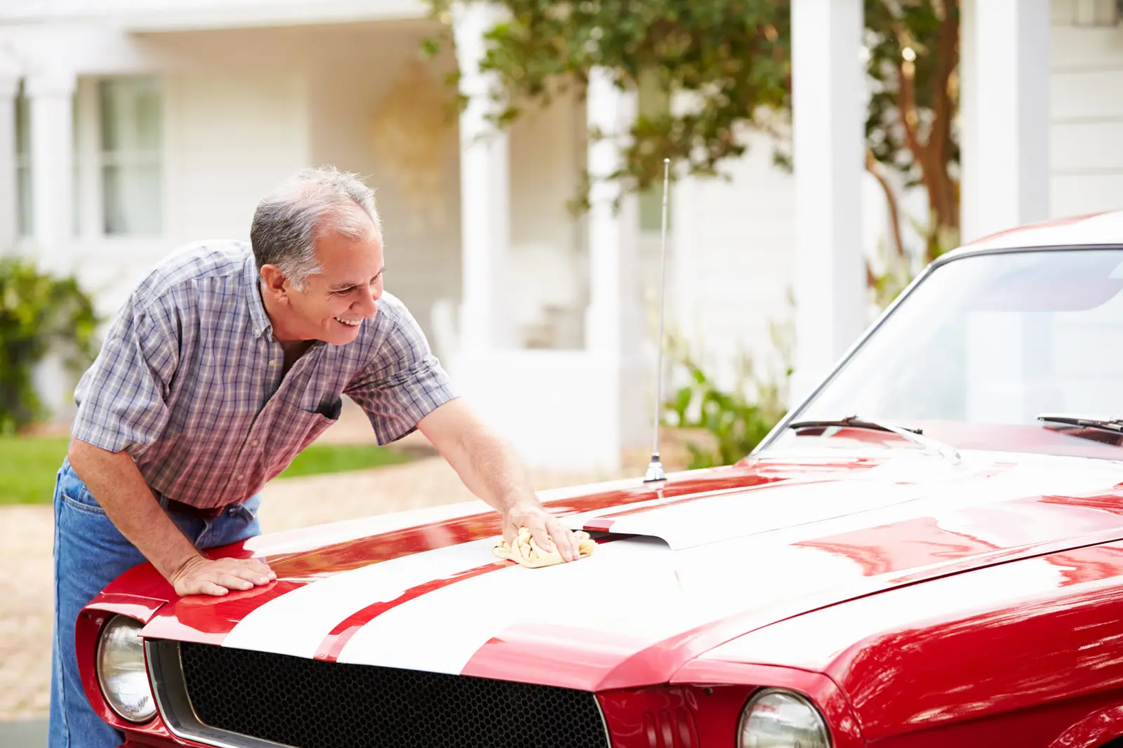 A man cleaning the bonnet of a red classic car on his driveway